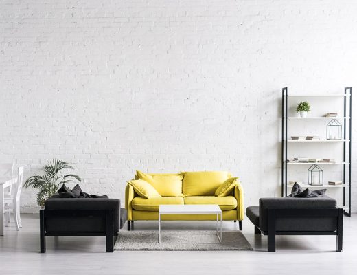 Salón minimalista de estilo industrial. Muebles de líneas marcadas de madera natural combinados con elementos de acero. Pared ladrillo visto. Sofá amarillo combinado con sillones negros.