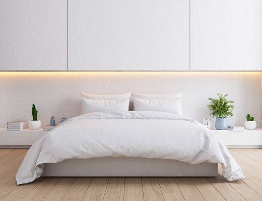 Dormitorio acogedor. Vista frontal cama vestida con relleno nórdico blanco y decoración con plantas de invierno. Suelo de madera clara.