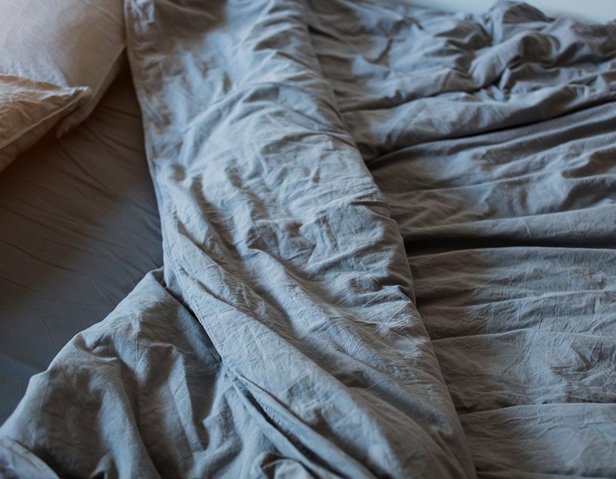 Primer plano cama deshecha con sábanas en tonos grises