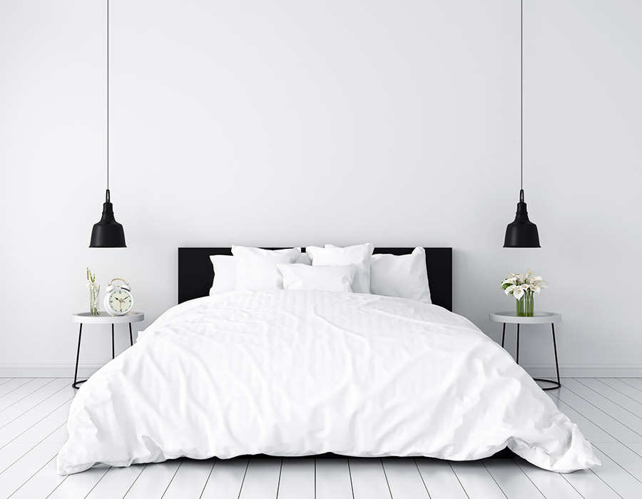 Dormitorio blanco. Vista frontal de la cama con ropa de cama en color blanco y almohadones en color blanco. Cabezal negro combinado con lámparas de noche en color negro. Suelo parquet blanco